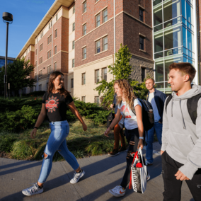 A student leader guides a group of students past University Suites.
